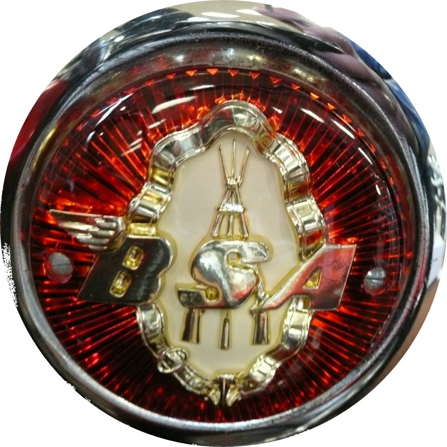 1957 BSA round tank badge: red sunburst ring around gold piled arms in a garter above a winged BSA on a cream ground