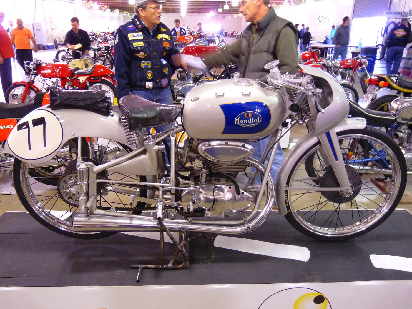 Restored FB Mondial 125 Bialbero racer with a silver tank and blue panel at a motorcycle show
