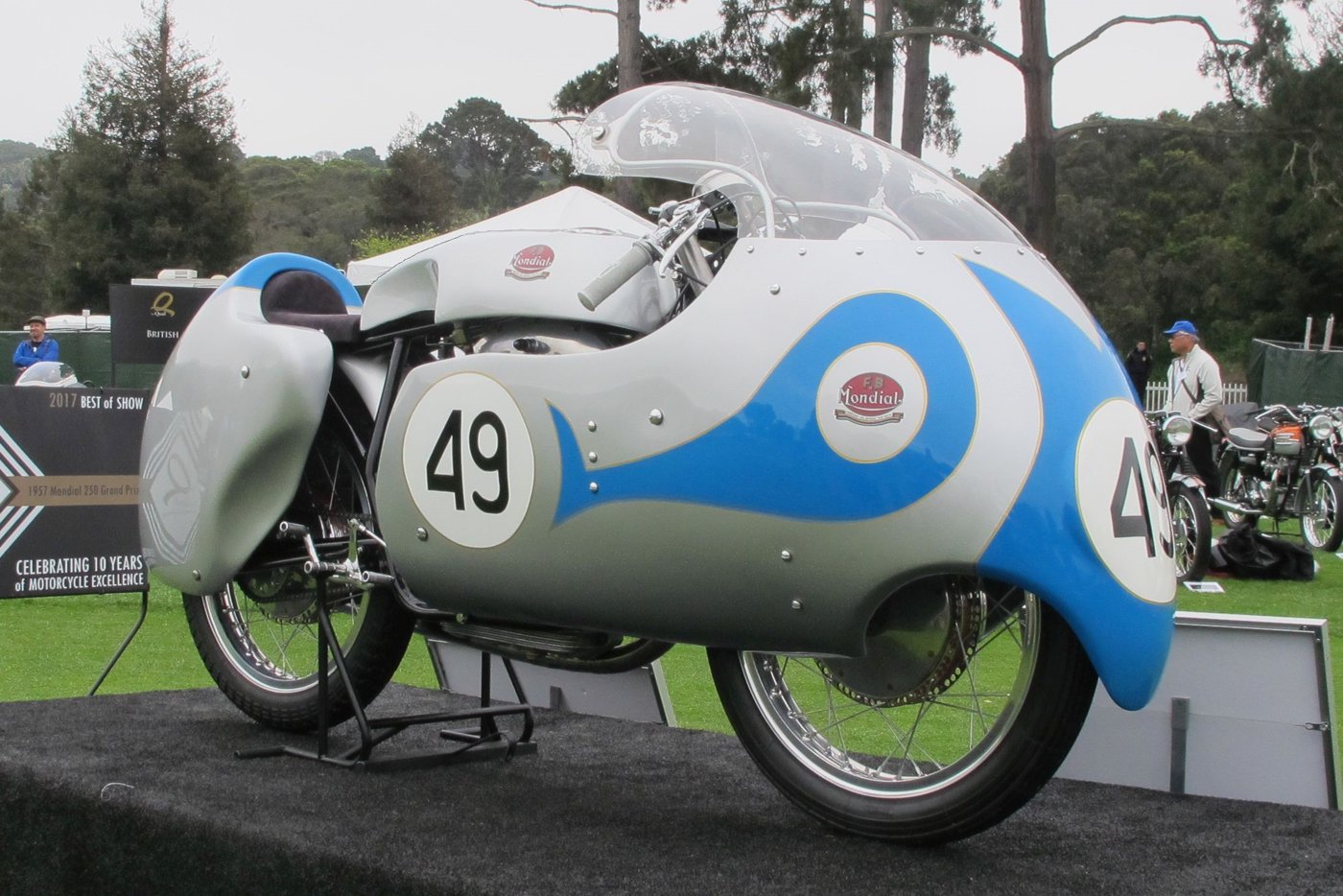 1957 Mondial 250 GP racer with a silver and light blue dustbin fairing, number 49, on display on a lawn