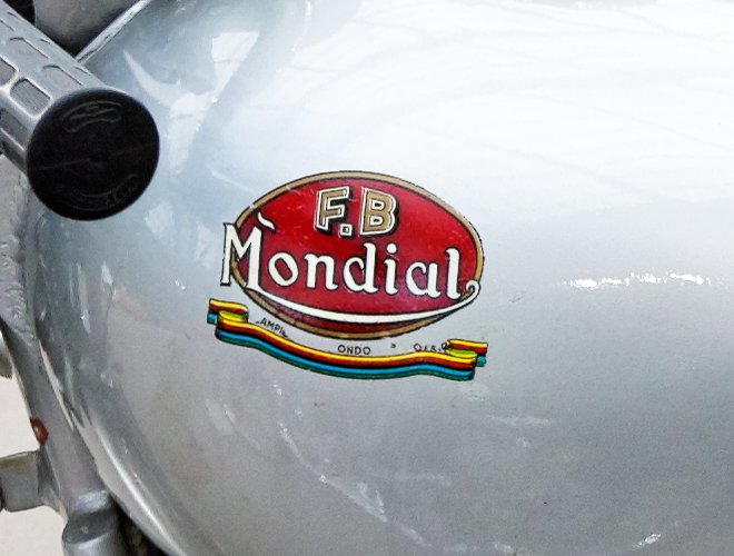 Worn red F.B Mondial tank transfer with a striped Campione del Mondo ribbon on a silver tank