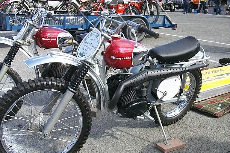 Two 1960s Husqvarna motocross motorcycles with candy-red tanks, chrome knee panels and the Husqvarna script in white