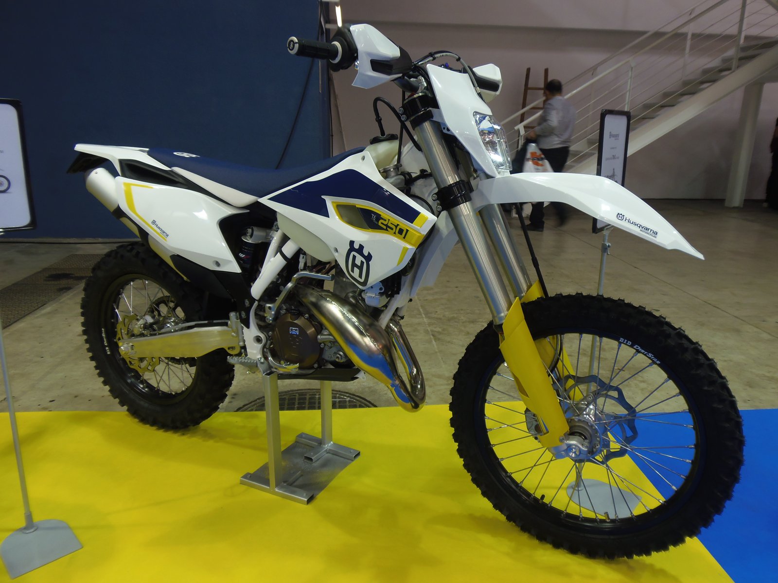 White 2015 Husqvarna TE 250 enduro with blue and yellow graphics and a large navy crown-H on its radiator shroud