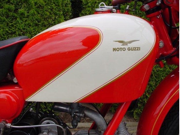 Red and cream tank of a 1954 Moto Guzzi Airone with a small gold eagle above gold MOTO GUZZI lettering