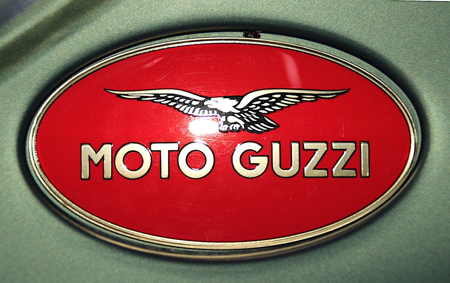 Raised red oval Moto Guzzi tank badge with a detailed gold and black eagle above gold MOTO GUZZI letters and a polished rim