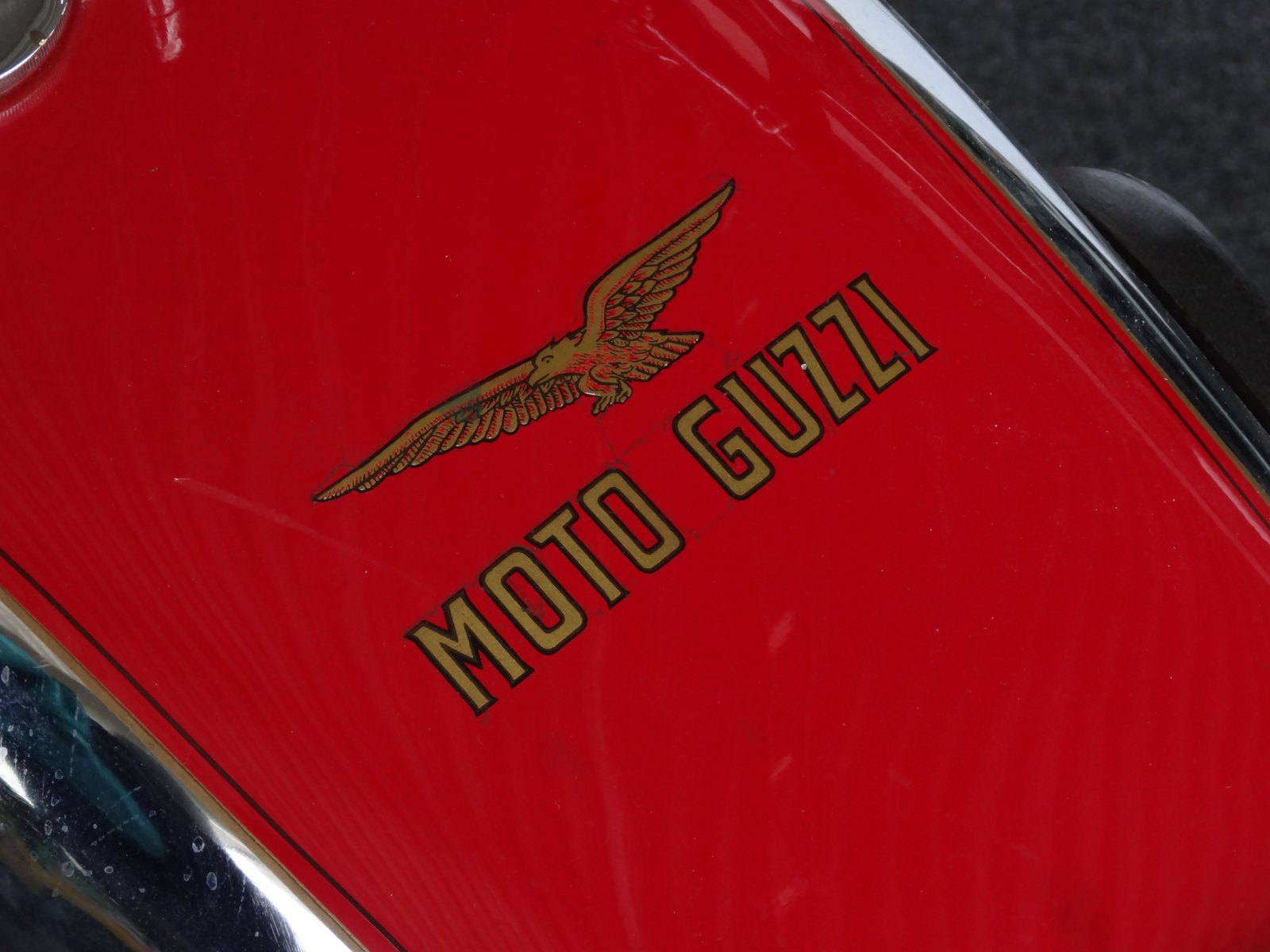 Close-up of a red Moto Guzzi tank with a gold-outlined eagle above large gold MOTO GUZZI lettering set at an angle
