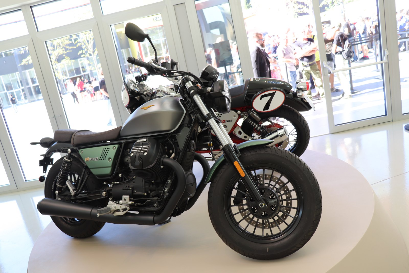 Moto Guzzi V9 Bobber Centenario with a satin metal and green tank carrying a gold eagle, on display at the Moto Guzzi museum