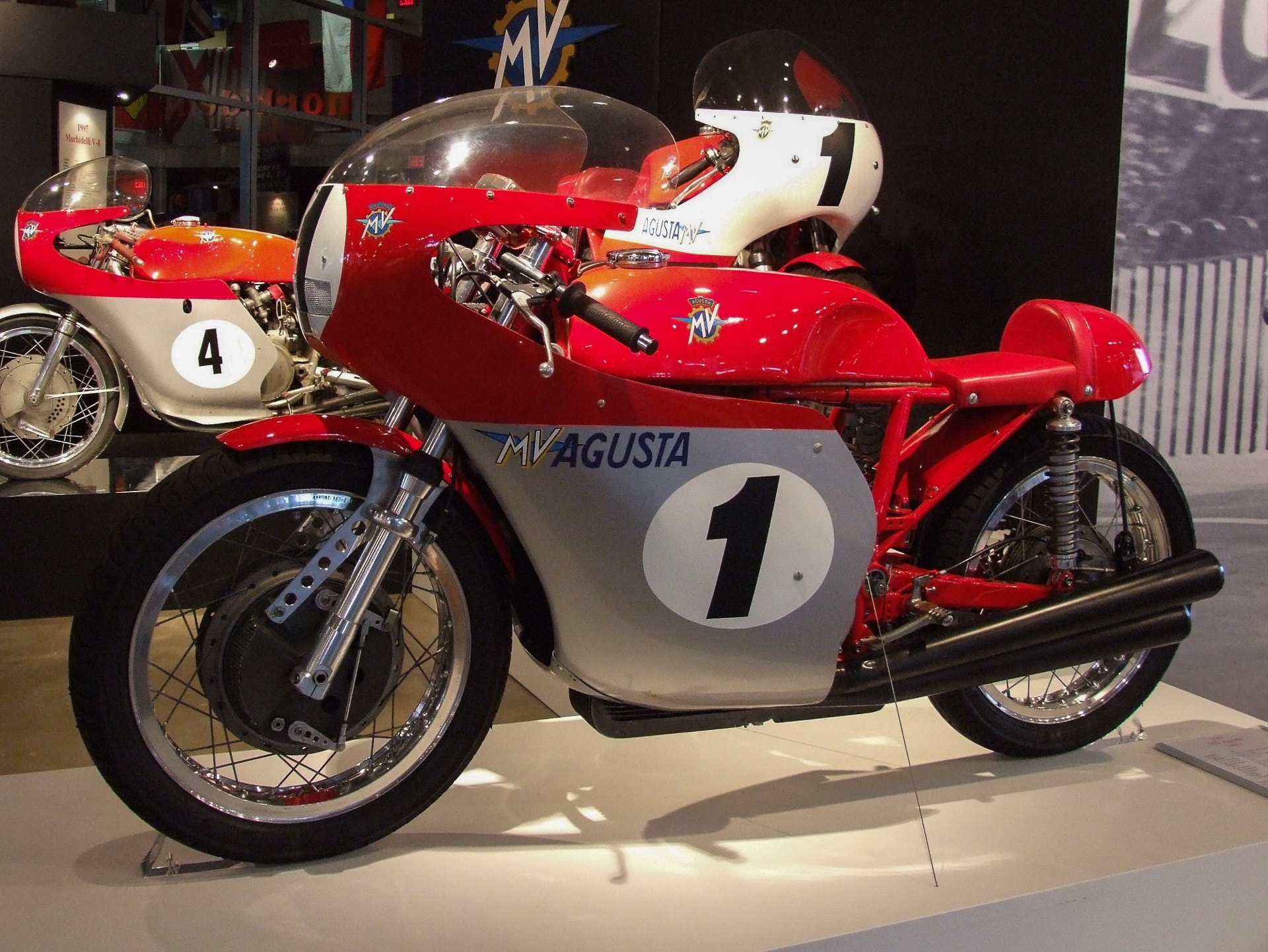 A red and silver 1967 MV Agusta 500 three-cylinder racer in a museum, with MV AGUSTA lettering on the silver fairing beside a white number 1 roundel