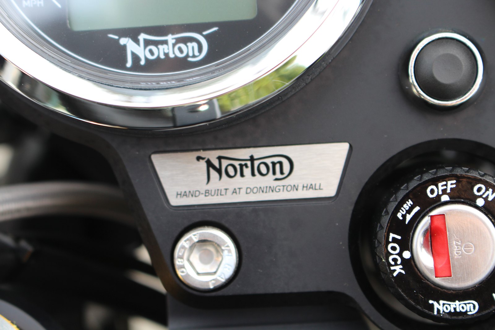 Close-up of a 2014 Norton Commando SF 961 with a brushed aluminium plate reading Norton, Hand-built at Donington Hall, below a speedometer that also carries the curly N