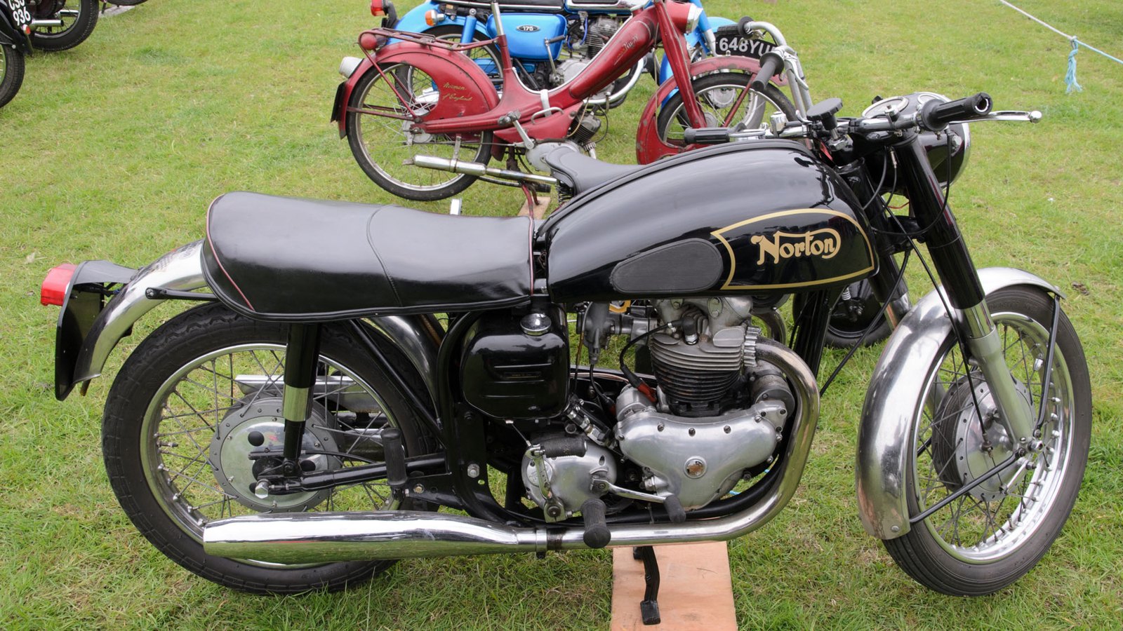 A 1956 Norton Dominator Model 88 with a black tank carrying a gold curly N Norton transfer inside a gold-lined panel