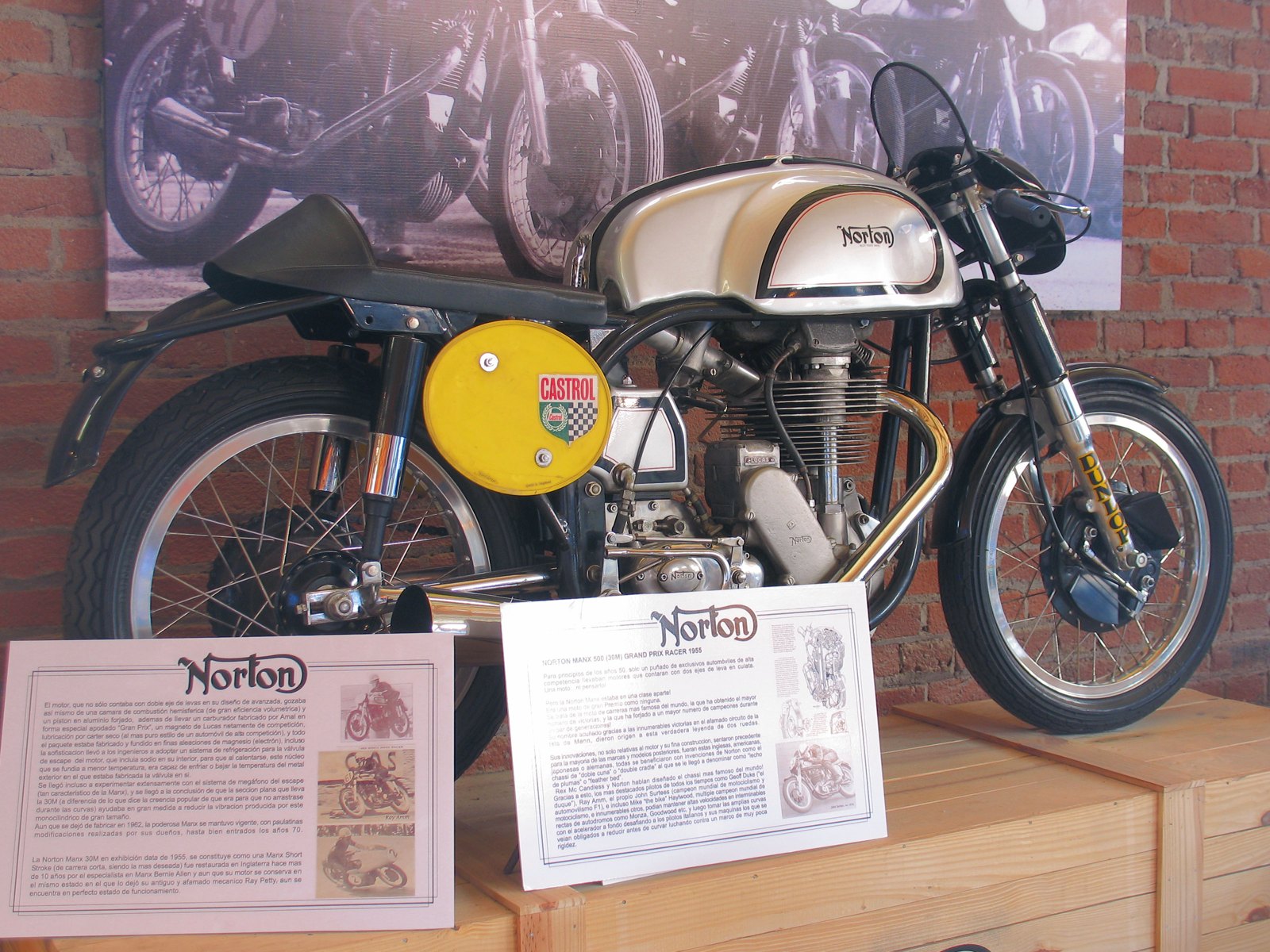 A 1955 Norton Manx 30M racer in a museum, with a silver tank carrying a black curly N inside a black and red lined panel