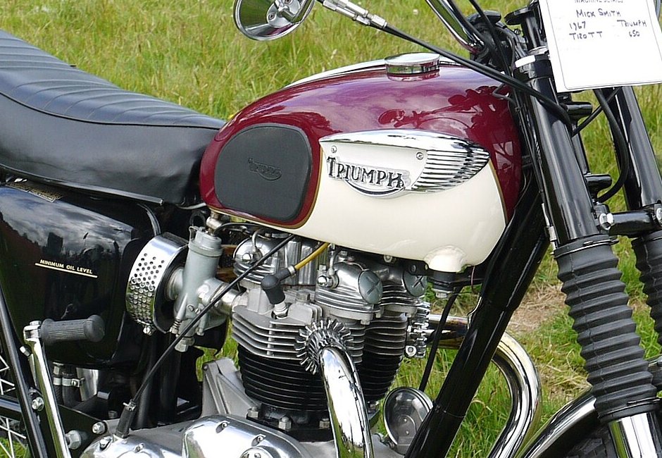 Aubergine and white tank of a 1967 Triumph T120 Bonneville with a chrome eyebrow badge arching over the TRIUMPH wordmark