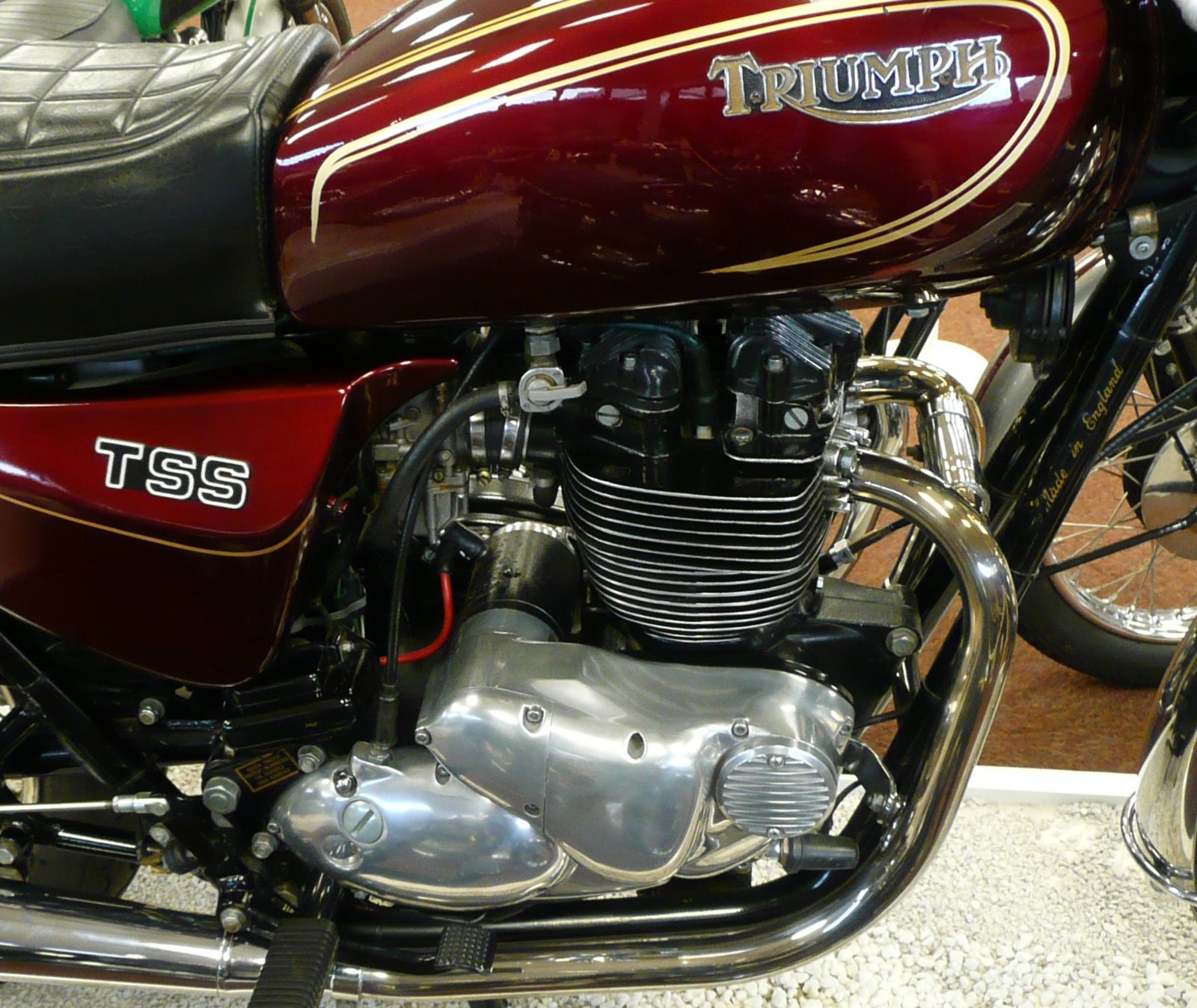 Maroon tank and TSS side panel of a Triumph T140W TSS with a cast gold and black TRIUMPH badge